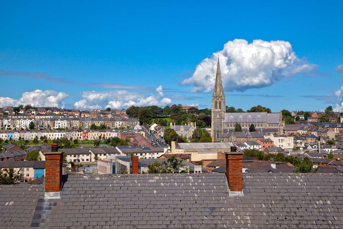 A rooftop view across Derry with terraced houses and a cathedral spire