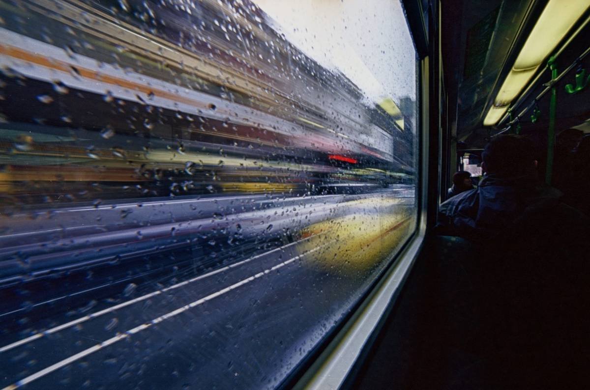Rain streaked bus window with motion blur and passengers inside
