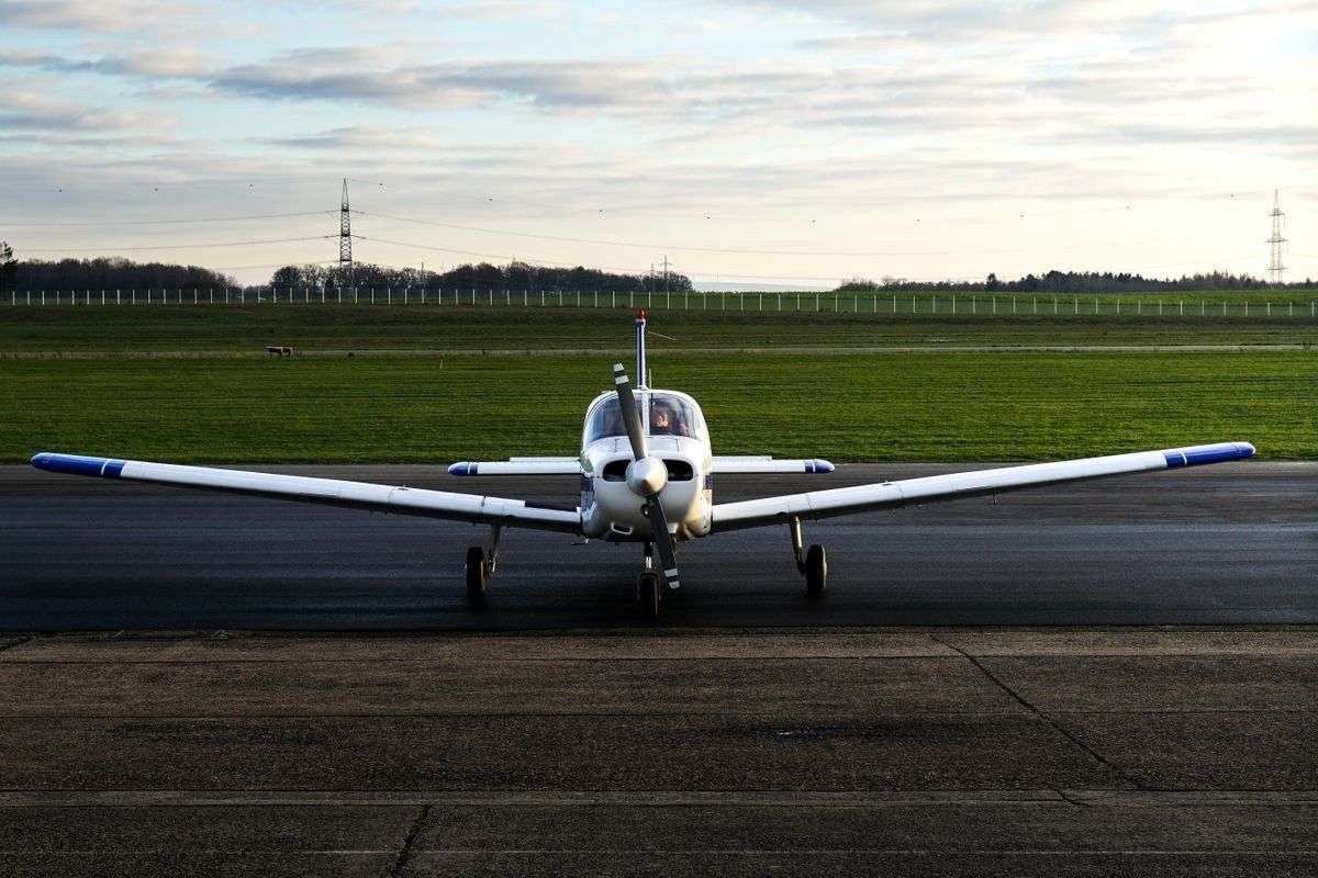 A small propeller plane parked on a runway beside green fields