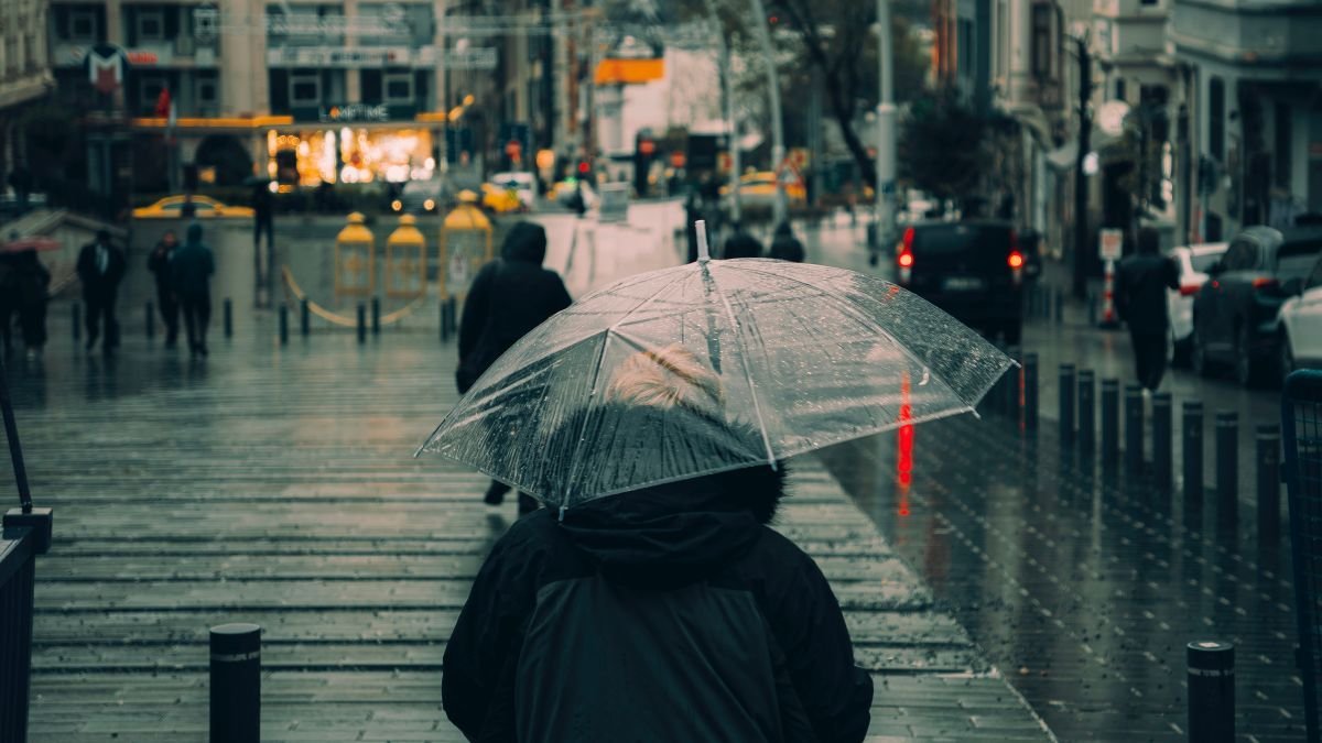 A person under a clear umbrella walking a wet grey city street in the rain