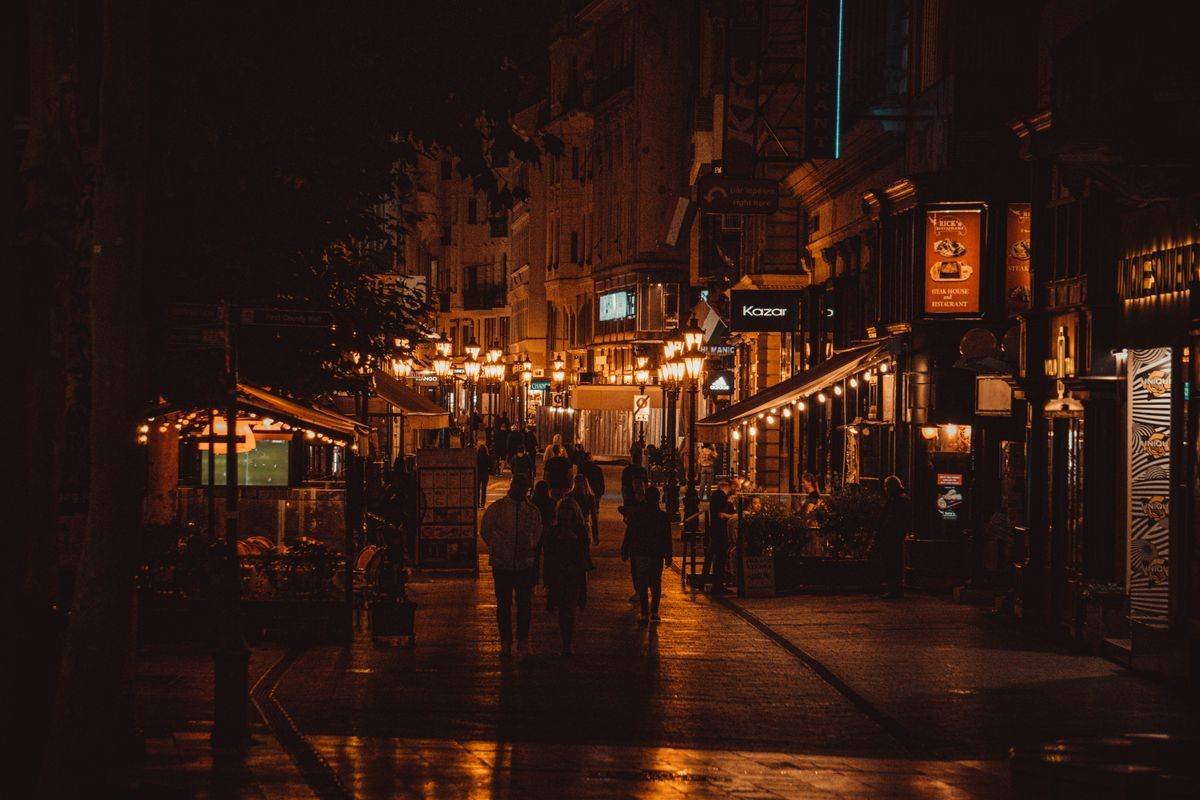 People walking a warm lamplit city street at night on wet pavement