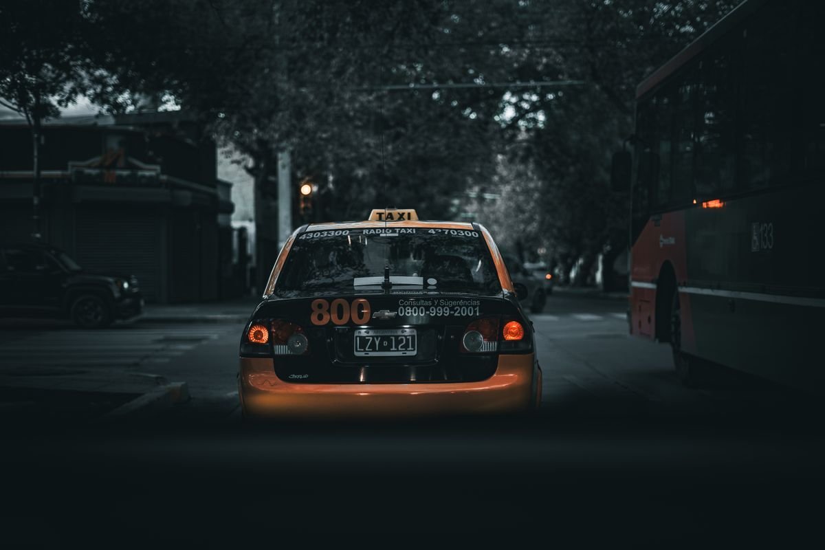 A taxi at night showing a lit roof sign and red tail lights on a dark street
