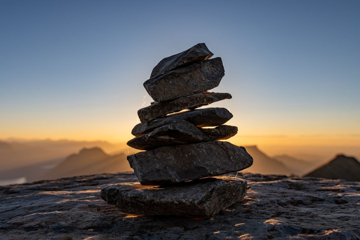 A stacked stone cairn on a mountain summit with sunset light behind