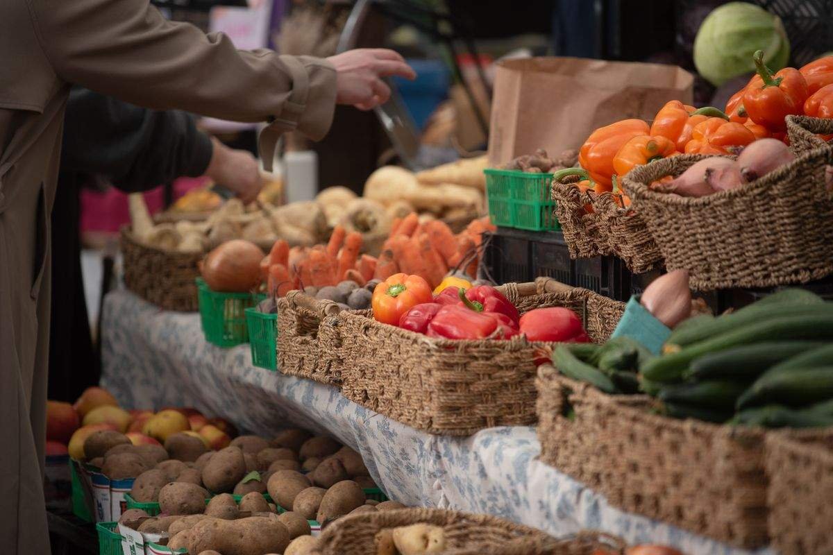 Baskets of fresh vegetables at a market stall with a shopper reaching in