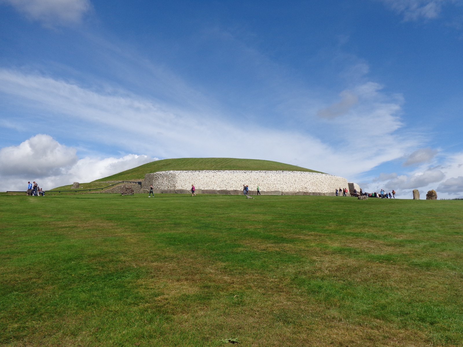 The grassed mound and white quartz front wall of Newgrange under a blue sky