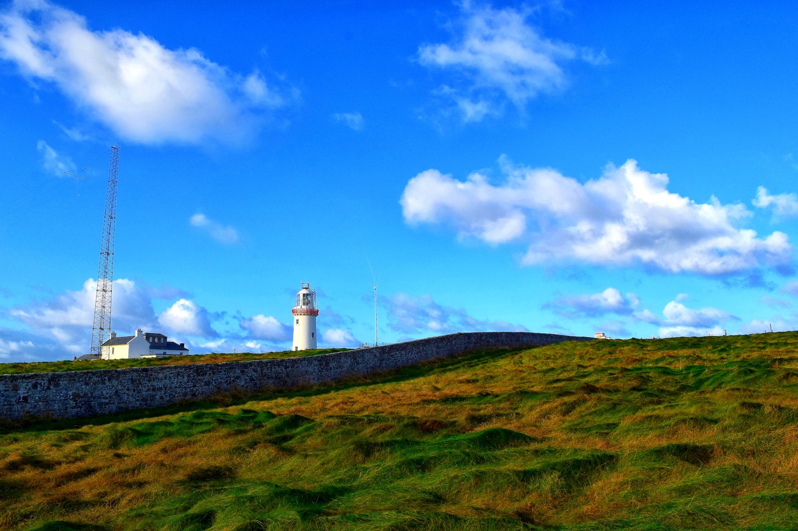 Loop Head Lighthouse standing white against a blue sky on the grassy headland at the tip of the Loop Head peninsula in County Clare