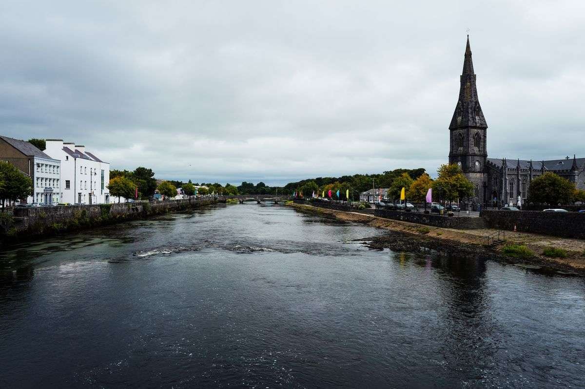 An Irish town along a river with quayside buildings and a church spire