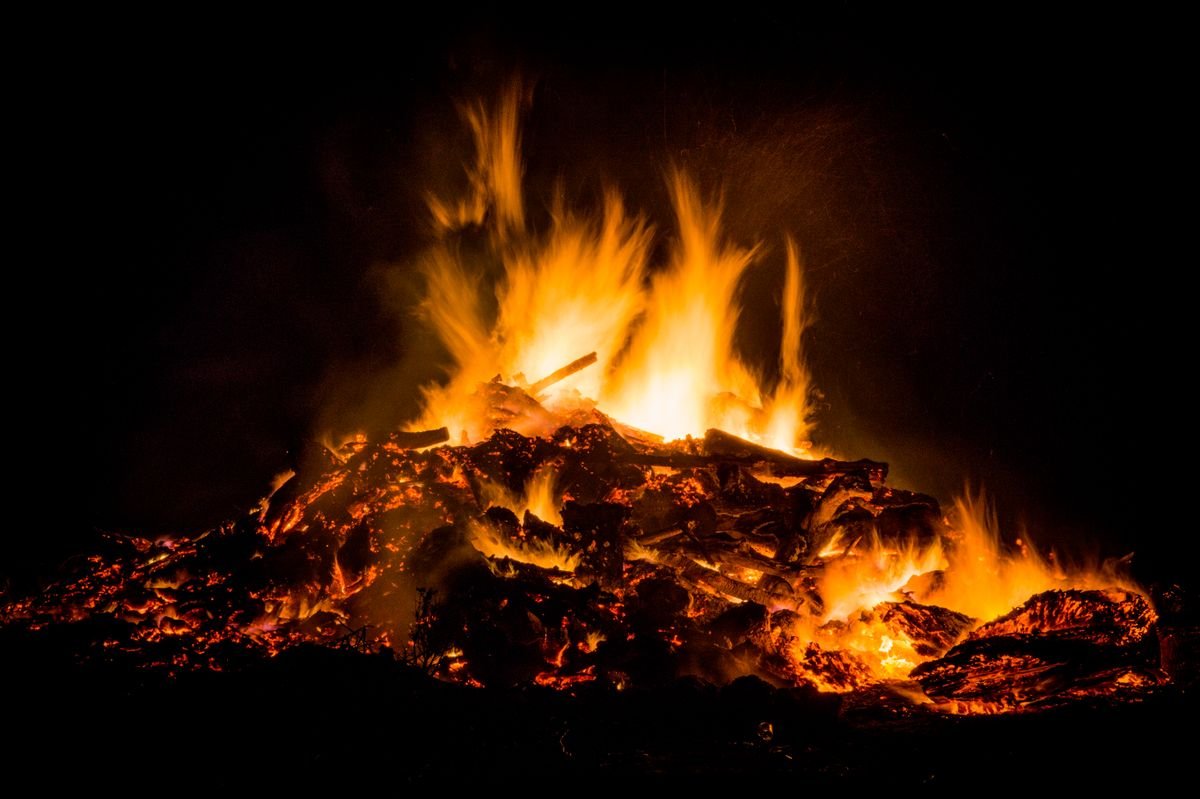 A large bonfire with tall flames burning against a black night sky