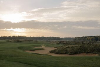 Links golfer playing out of a bunker among dunes and marram grass