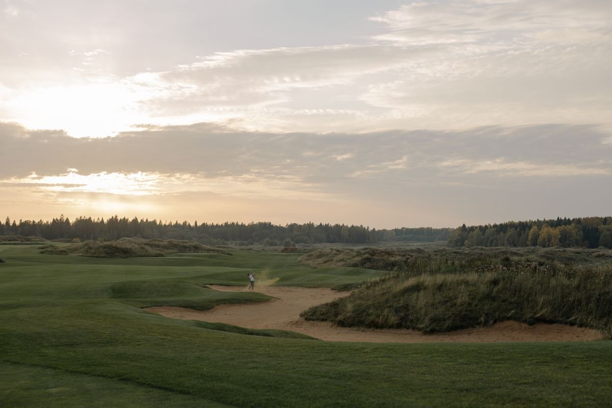 Links golfer playing out of a bunker among dunes and marram grass