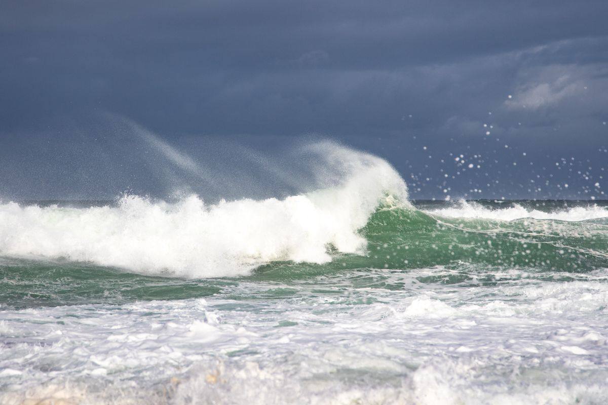 A powerful breaking wave with offshore spray under a dark stormy sky