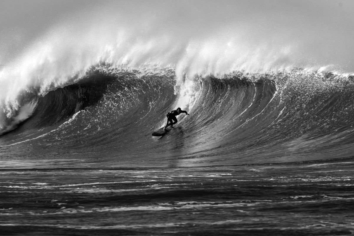 A surfer dropping into a huge wave in black and white