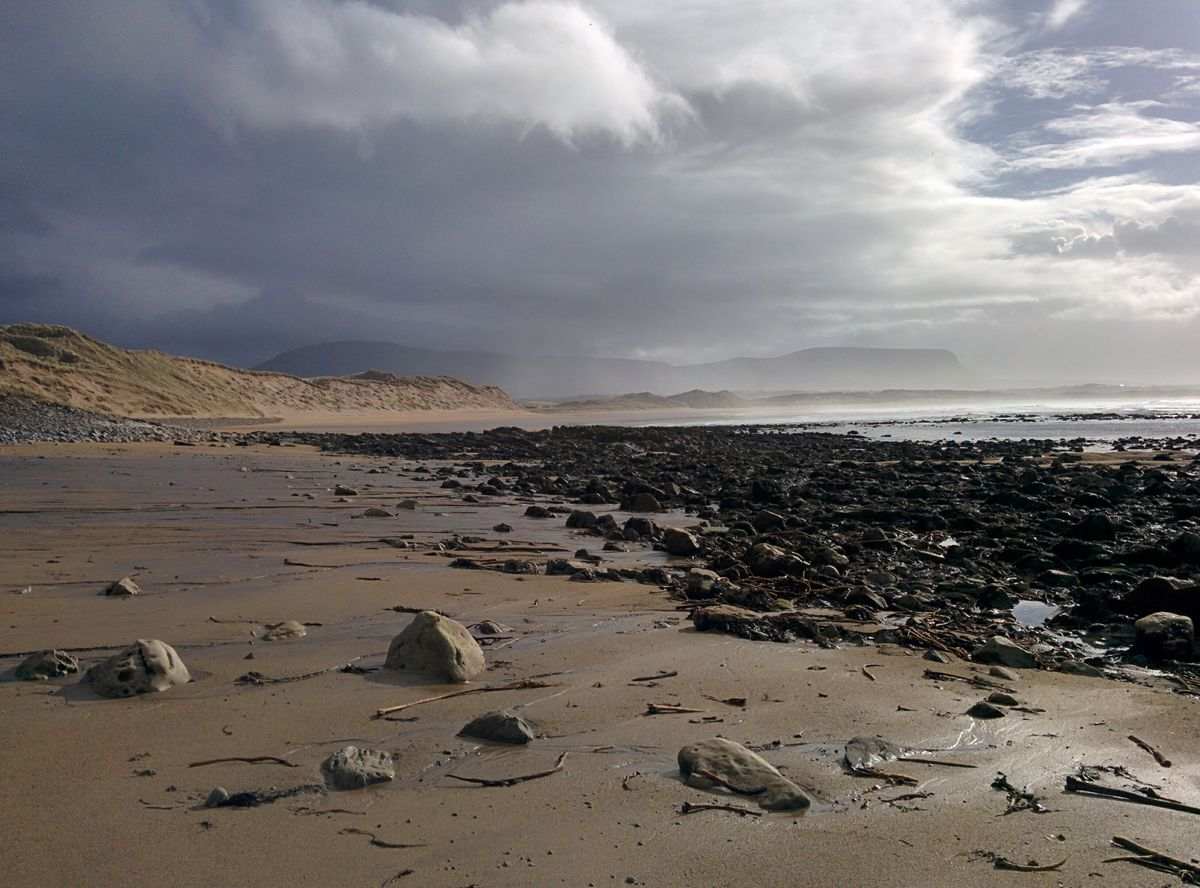 A rugged Sligo beach with dunes, a rocky shore and a mountain under a dramatic sky