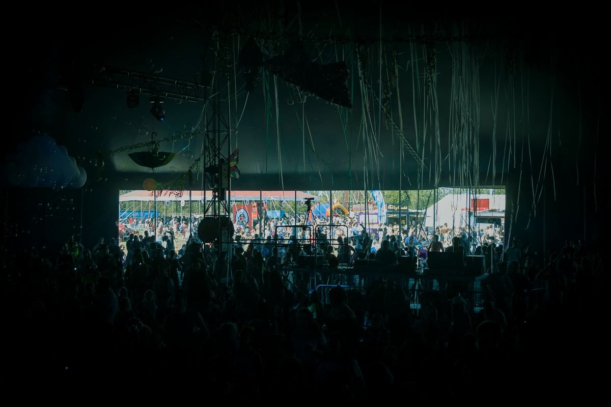 Crowd inside a tent at a music festival with a fairground beyond