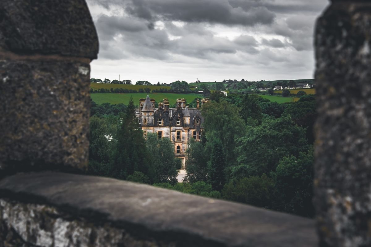 Gothic Irish castle framed through stone battlements under a grey sky