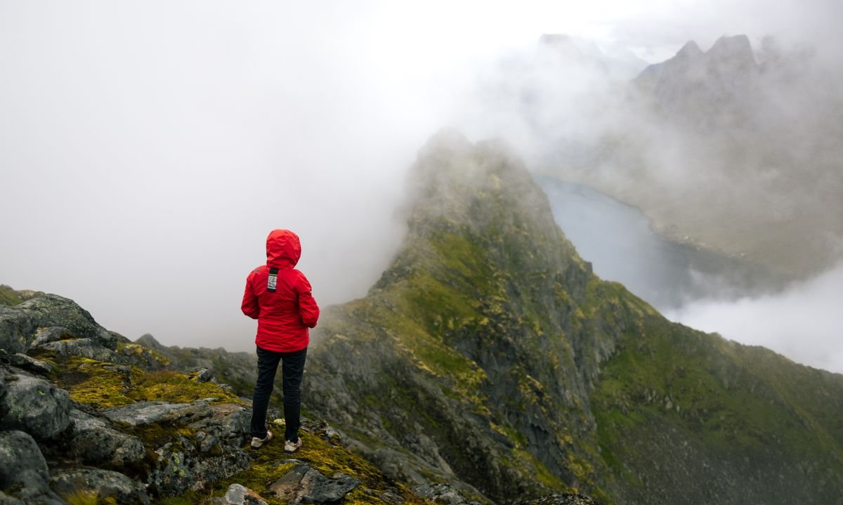 Hiker in a red rain jacket on a misty green mountain