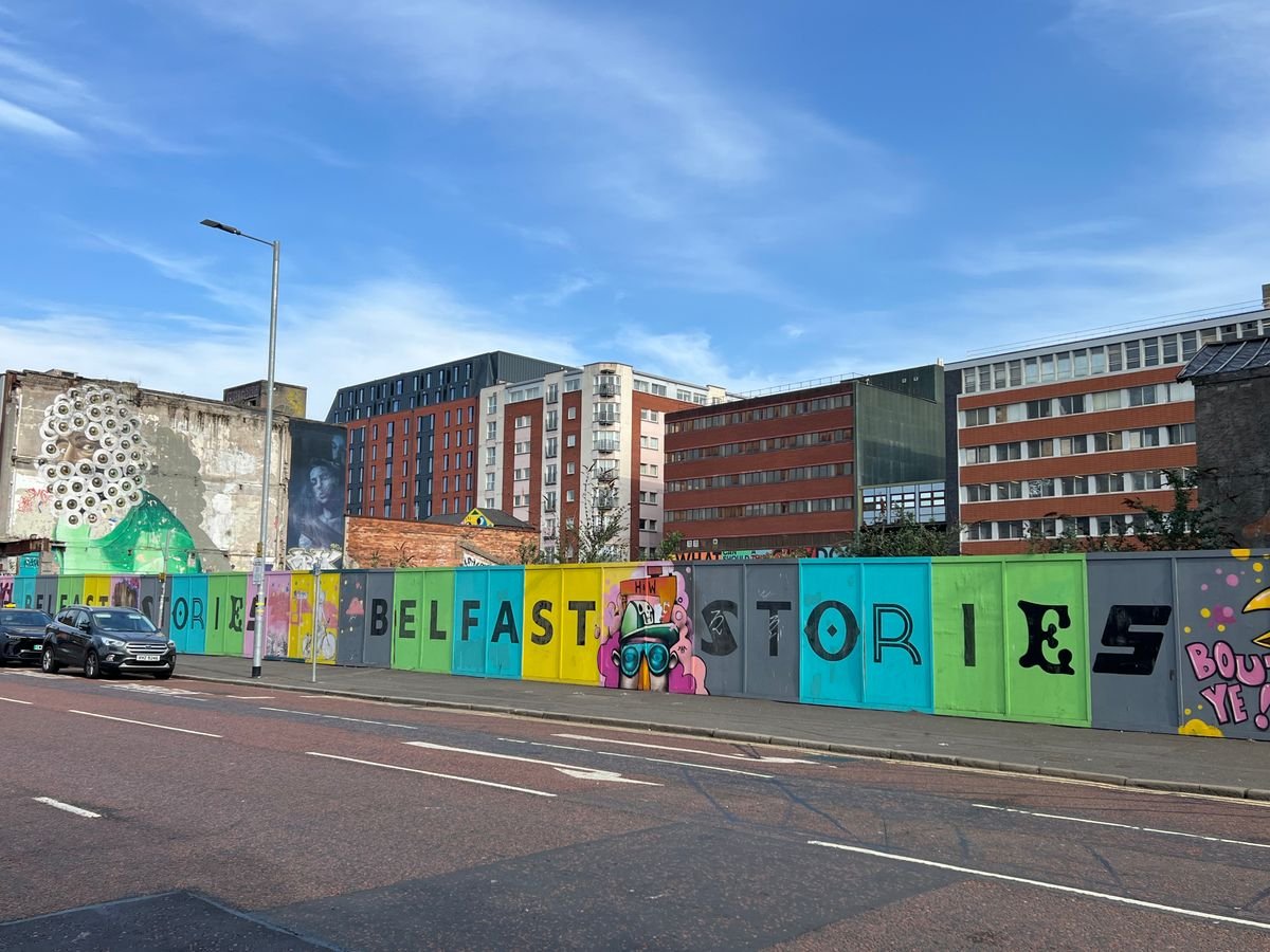 A colourful Belfast street art wall reading Belfast Stories with the city behind