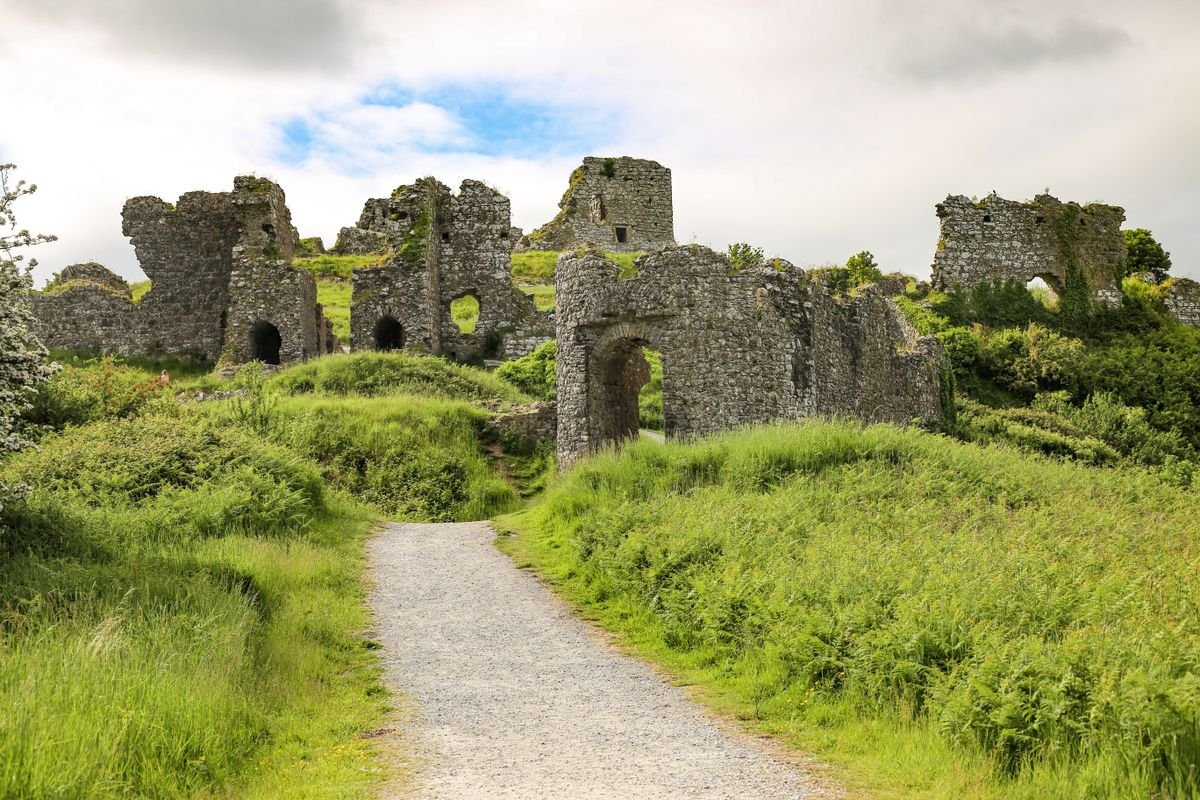 A stone castle ruin with a path leading up through green Irish countryside
