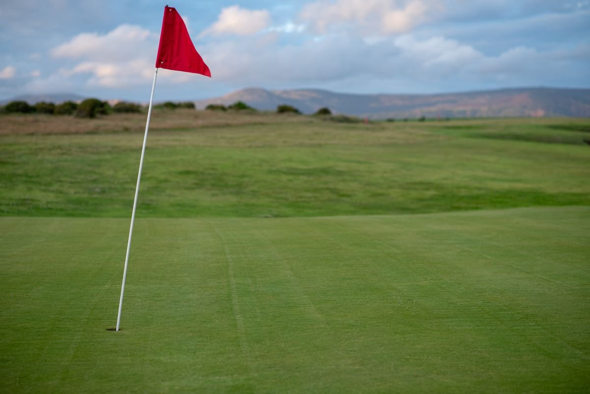 Links green with a red flag and rough grass under distant hills