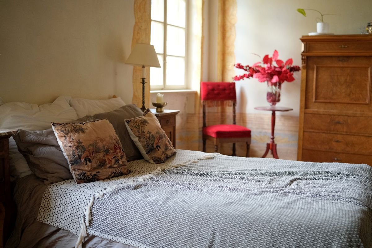 A warm traditional guesthouse bedroom with a made bed and antique dresser