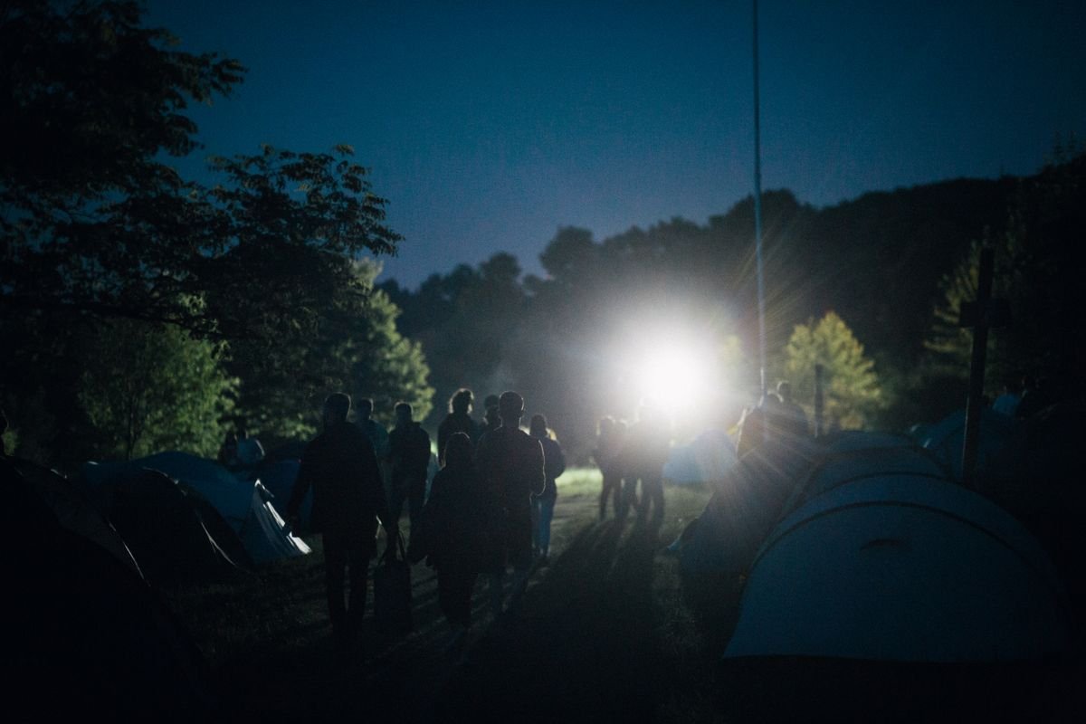 People walking through a festival campsite of tents at dusk