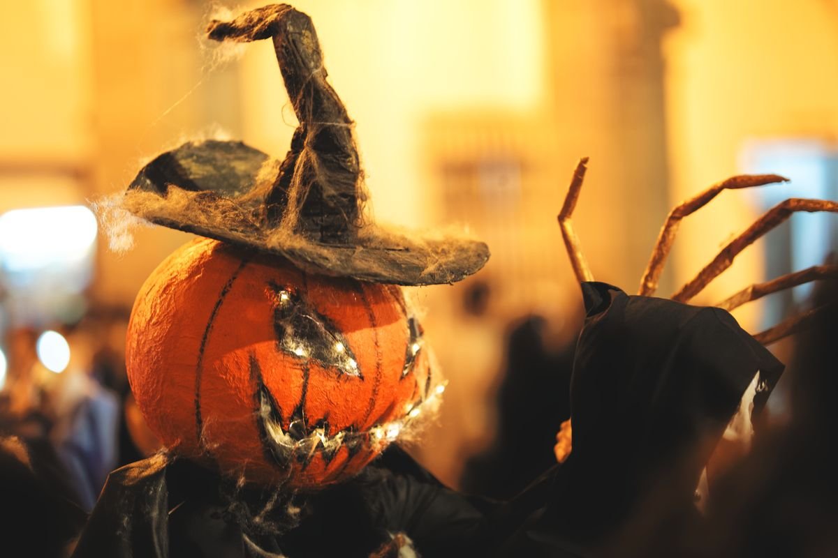 Pumpkin-headed costume figure lit up at a night Halloween festival