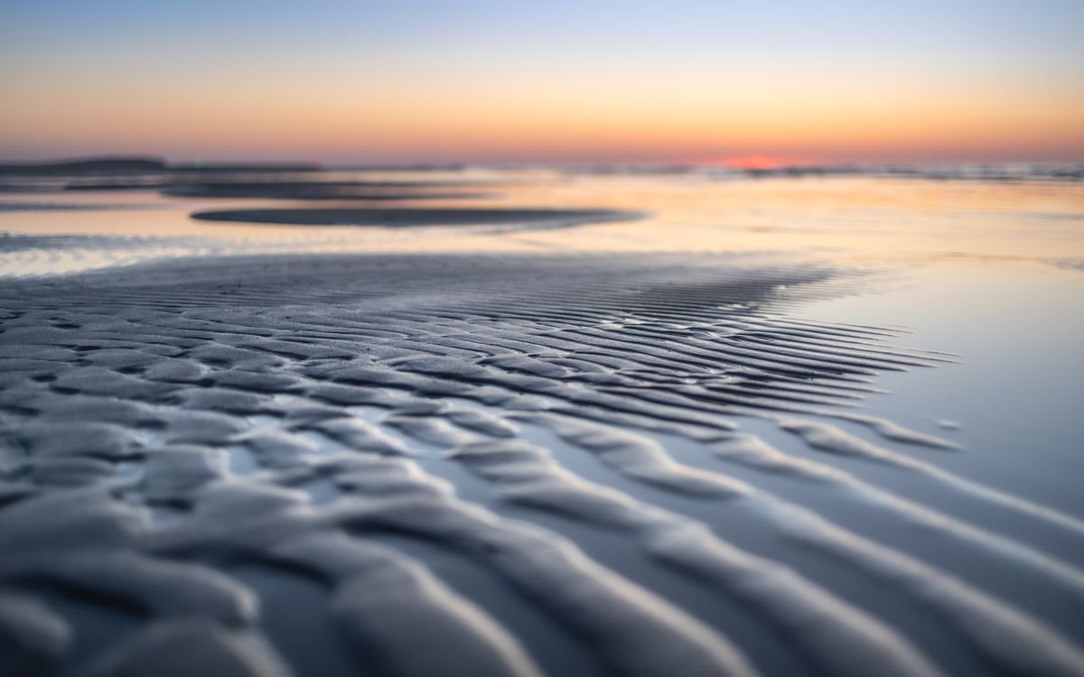 Low-tide wet sand reflecting a pastel sky