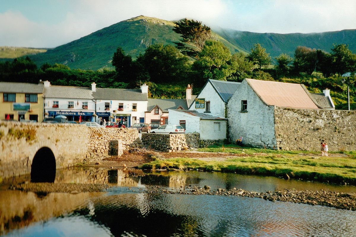 Irish village with a stone bridge and shops below a green hill