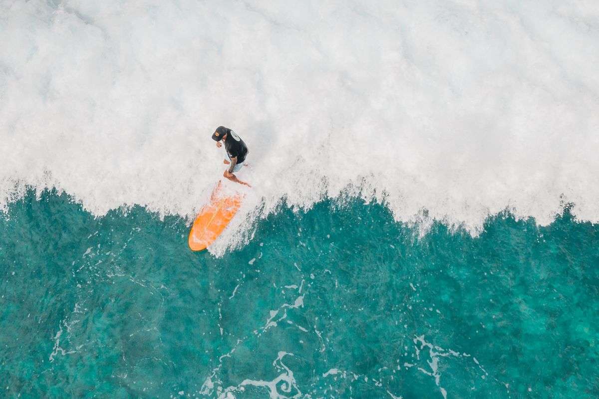 A surfer riding whitewater on an orange foam board seen from above