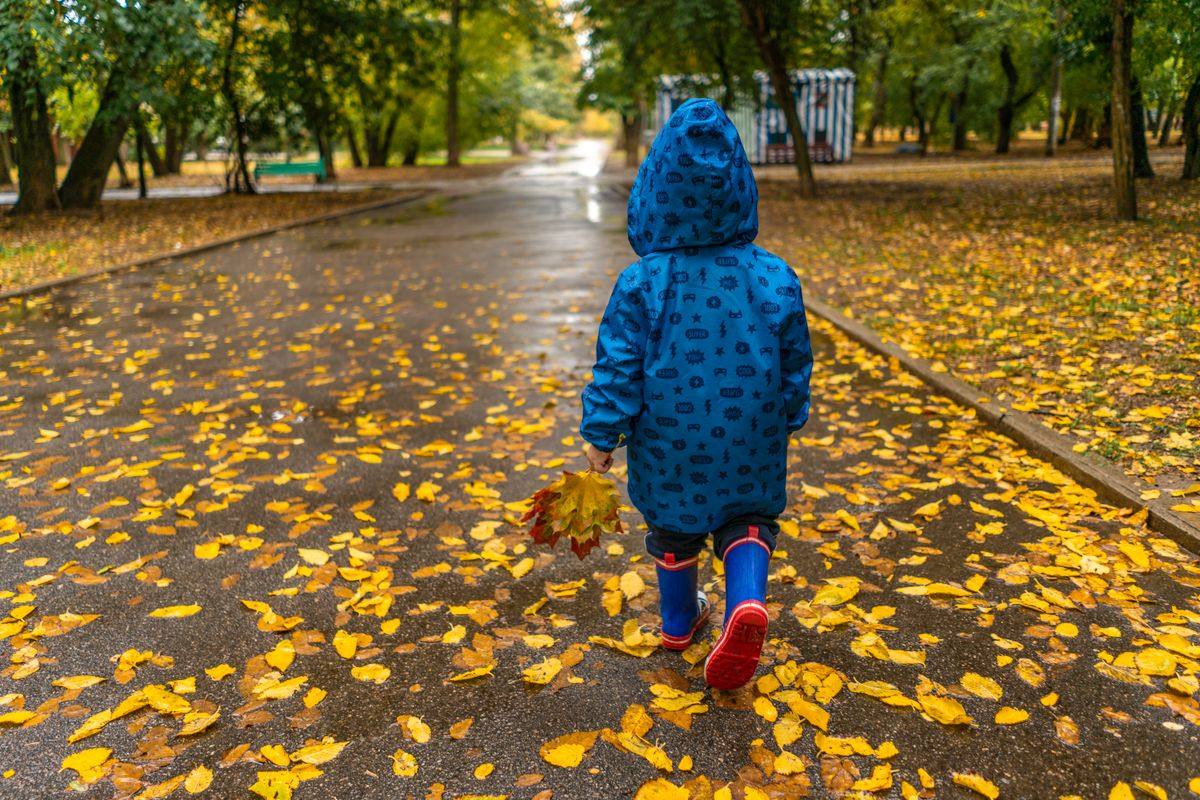 A child in a raincoat and wellies walking through autumn rain