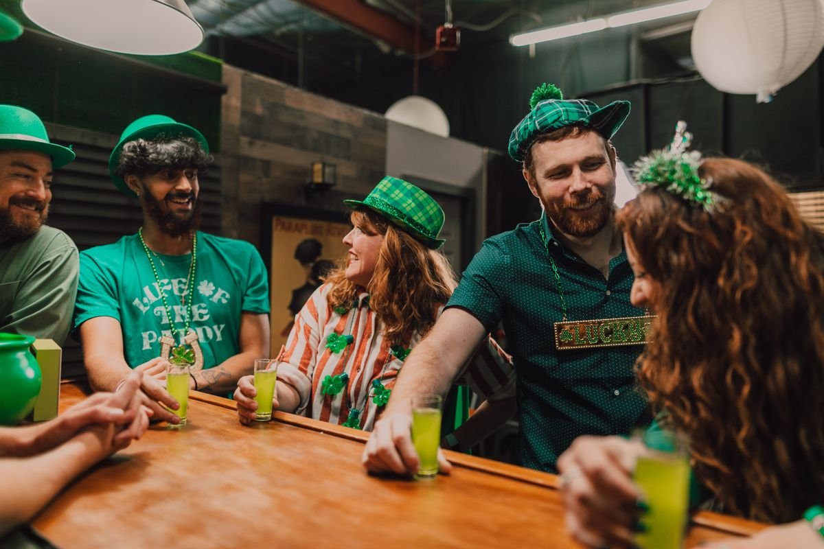 Friends in green St Patricks Day hats laughing over drinks at a bar