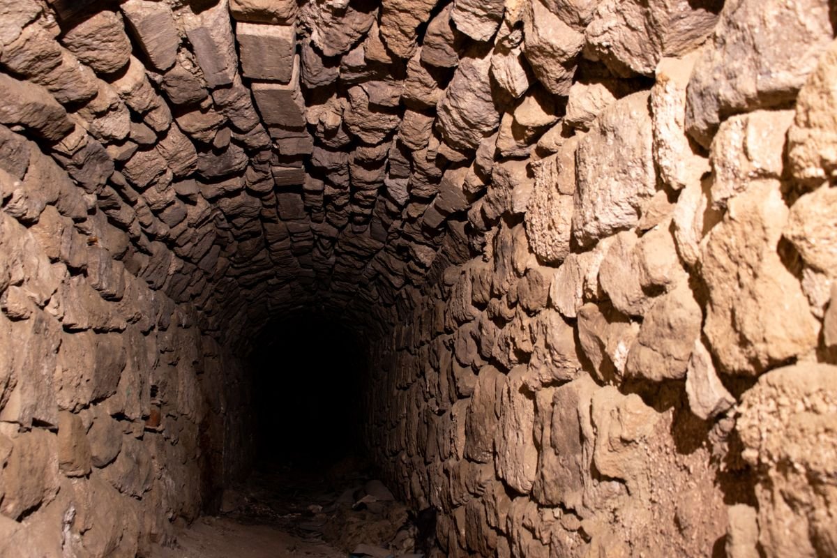 A narrow ancient stone passage running into darkness, like the tomb passage at Newgrange