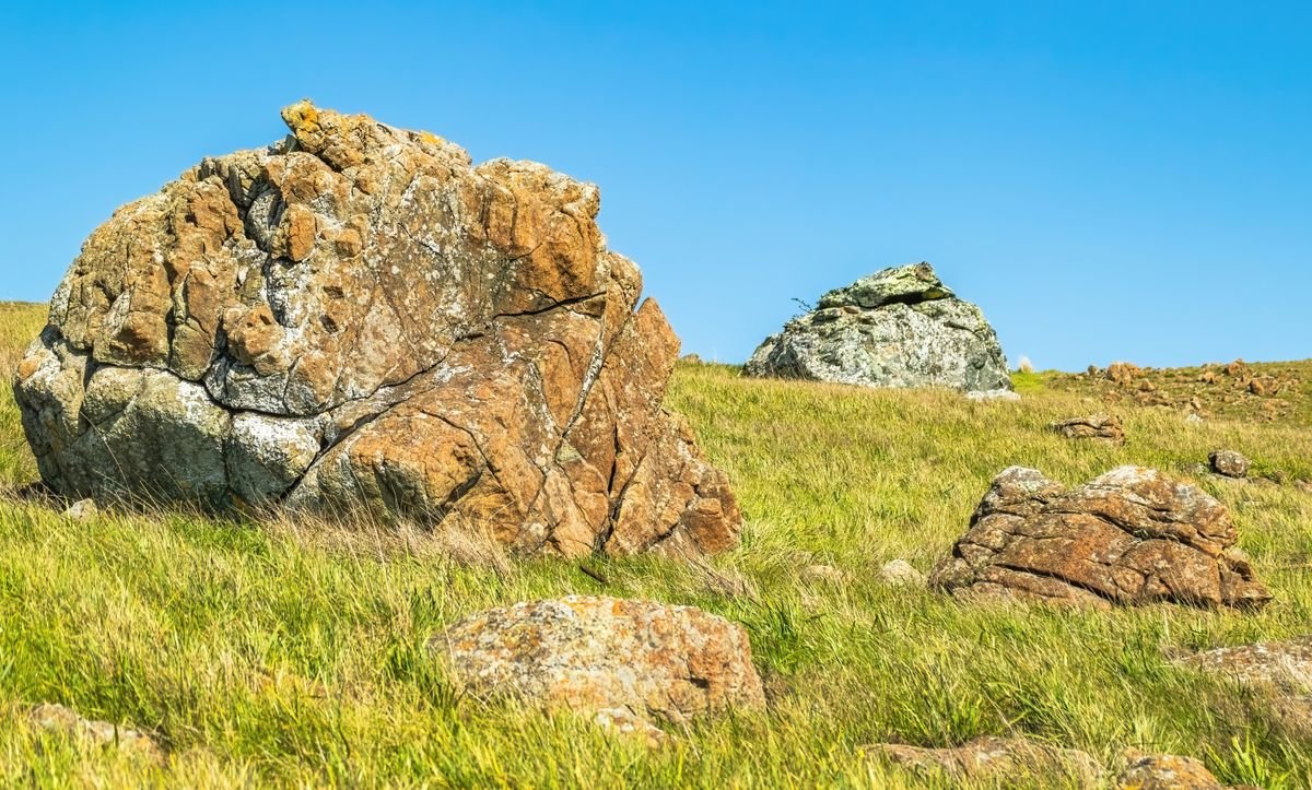 A large split boulder sitting in a grassy field under a clear sky at the Hill of Uisneach