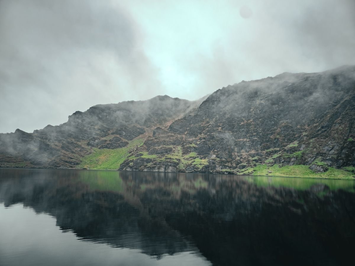 A moody mountain summit lake under a grey misty sky