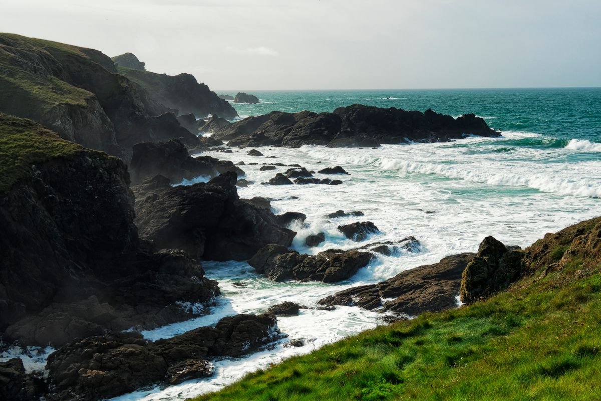 Waves breaking on rocks below a green clifftop on a rugged stretch of Irish coast