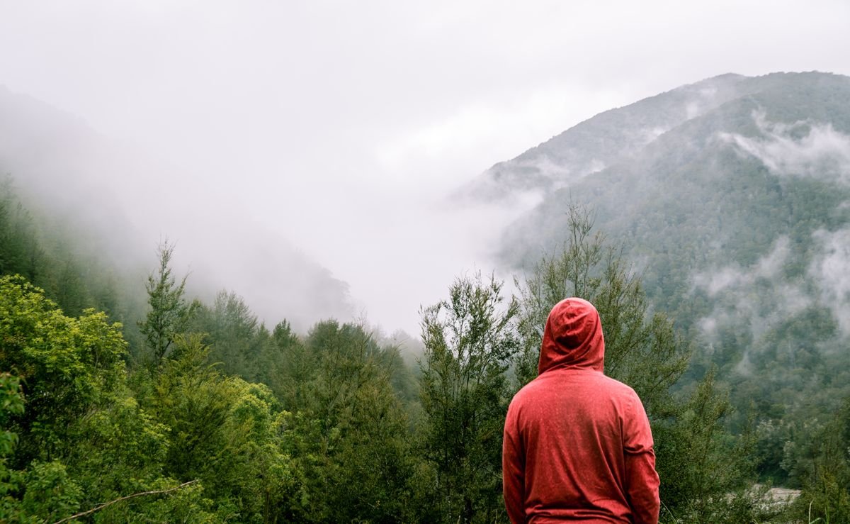 Person in a red rain hood facing misty green Irish hills