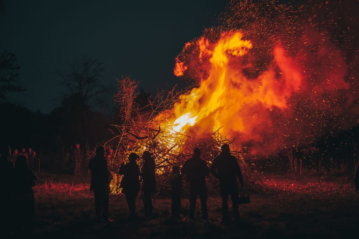 A large fire festival bonfire at night with a crowd of people silhouetted around it