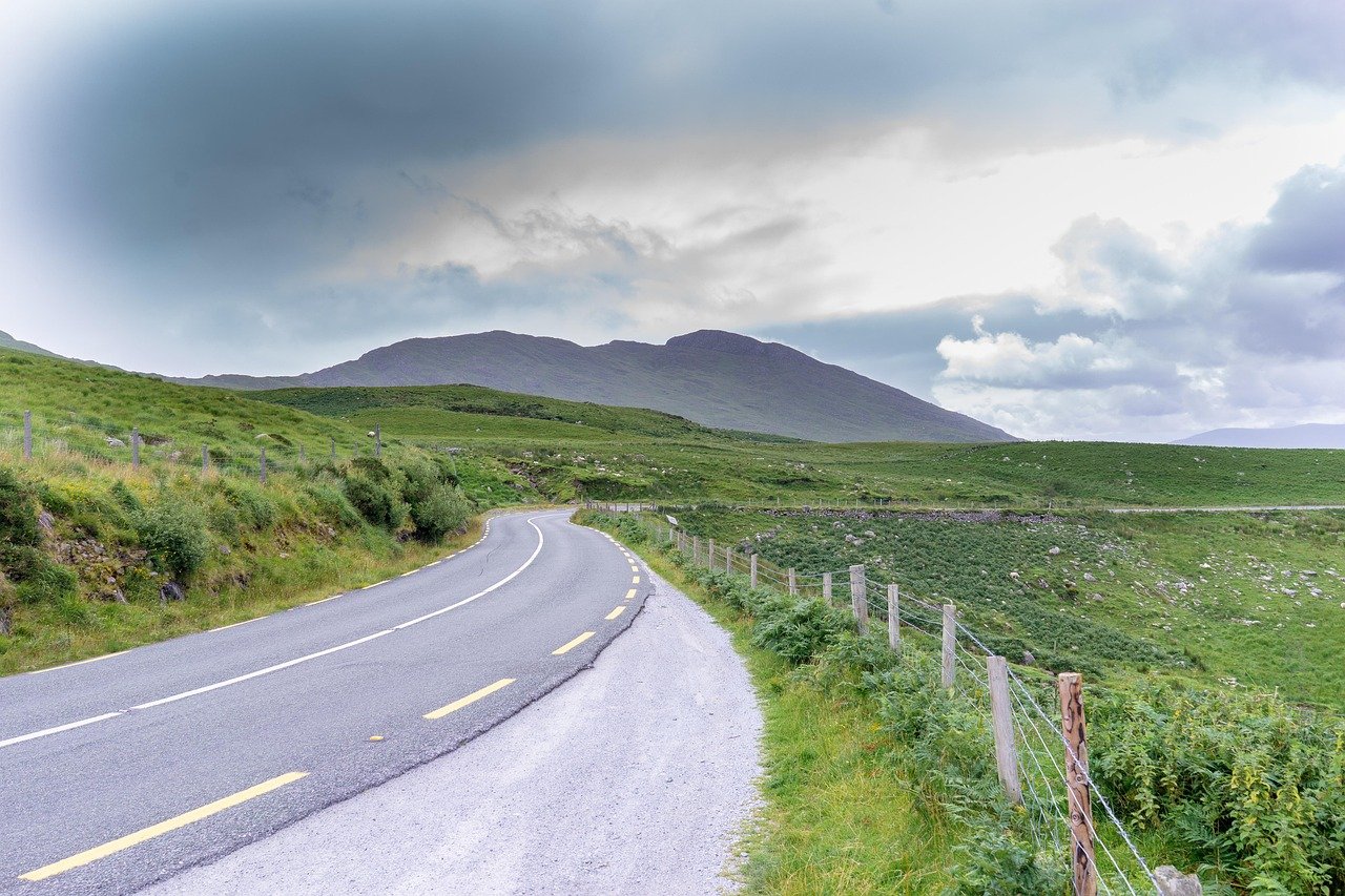 An empty Irish mountain road curving through green hills under a moody sky in Kerry