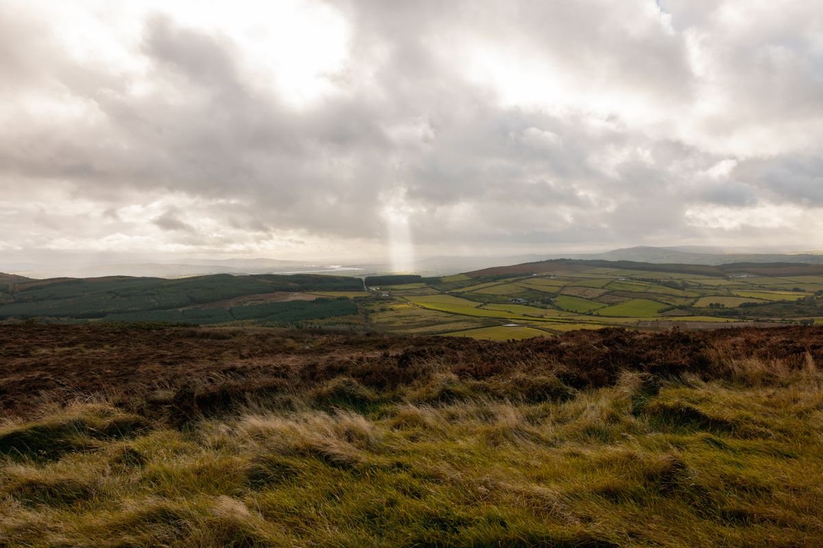 A moody upland with a shaft of light falling over green patchwork fields in County Tipperary