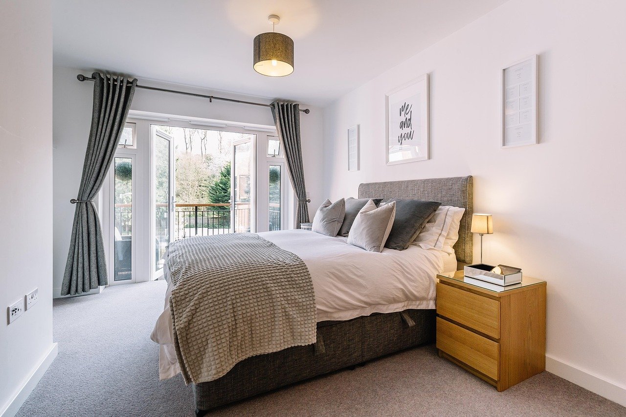 Bright made-up guest bedroom with a nightstand and balcony doors