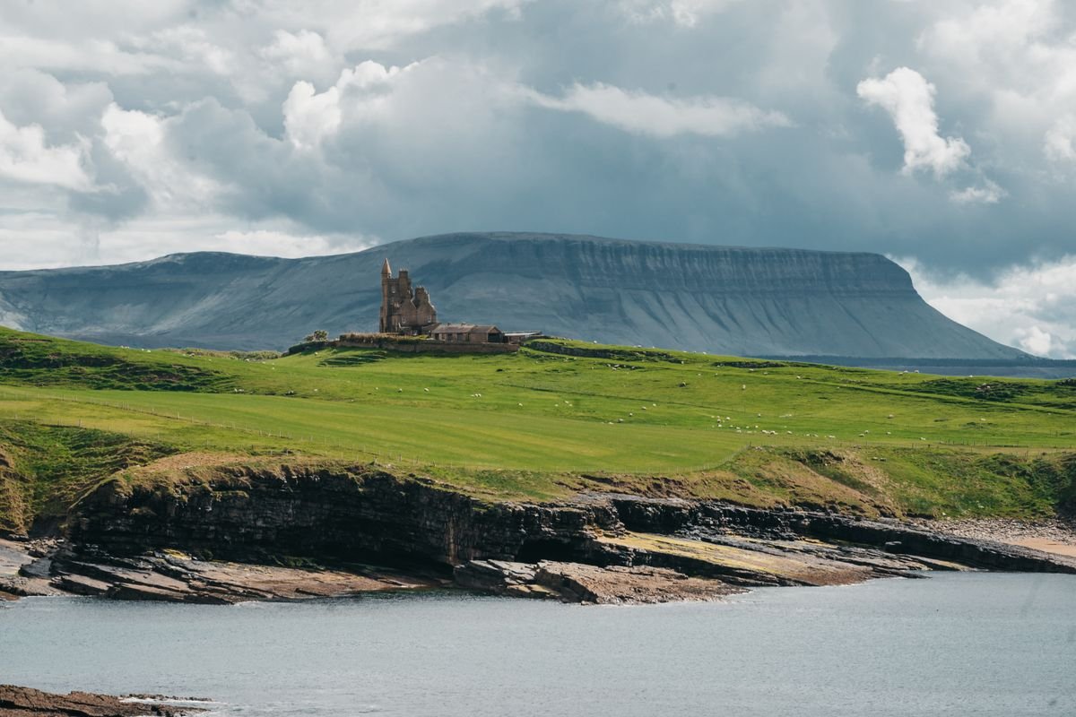 A castle on a green headland with a flat-topped mountain rising behind it