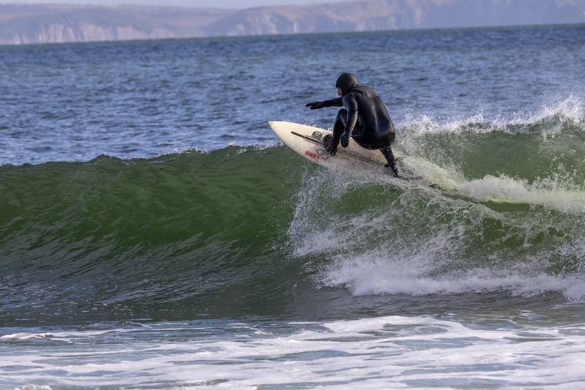 Surfer in a full black wetsuit riding a cold grey wave