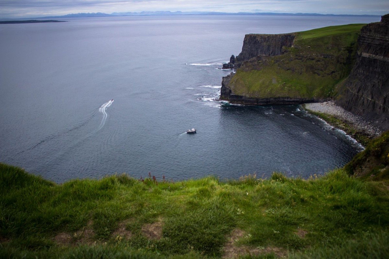 A small tour boat cruising along the base of the Cliffs of Moher