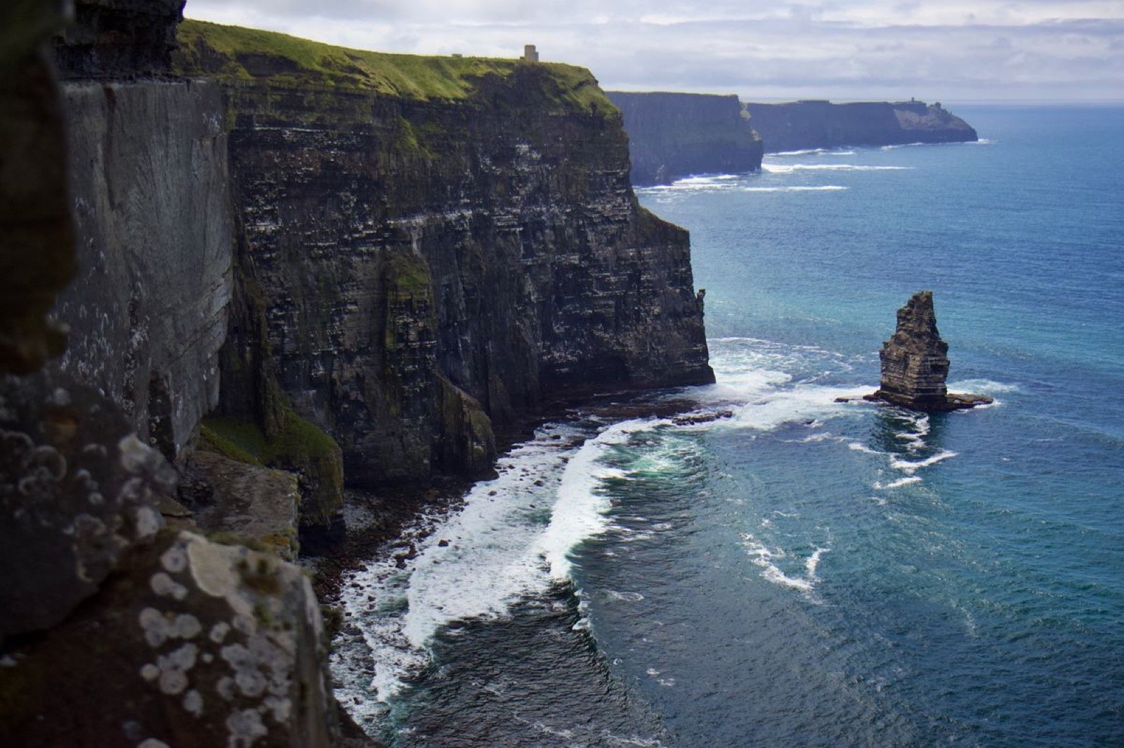 The Cliffs of Moher rising from churning surf with the sea stack, seen from the water