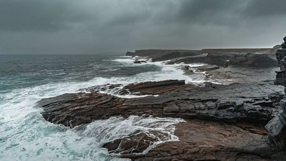 Waves crashing on dark limestone rock shelves under a grey stormy sky on the Clare coast in winter