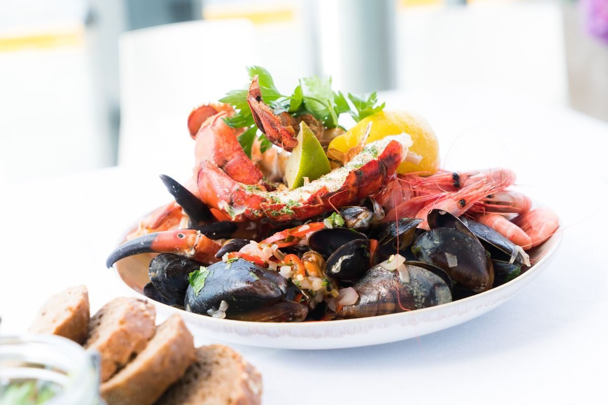 A seafood platter with lobster, mussels and prawns on a white plate with bread