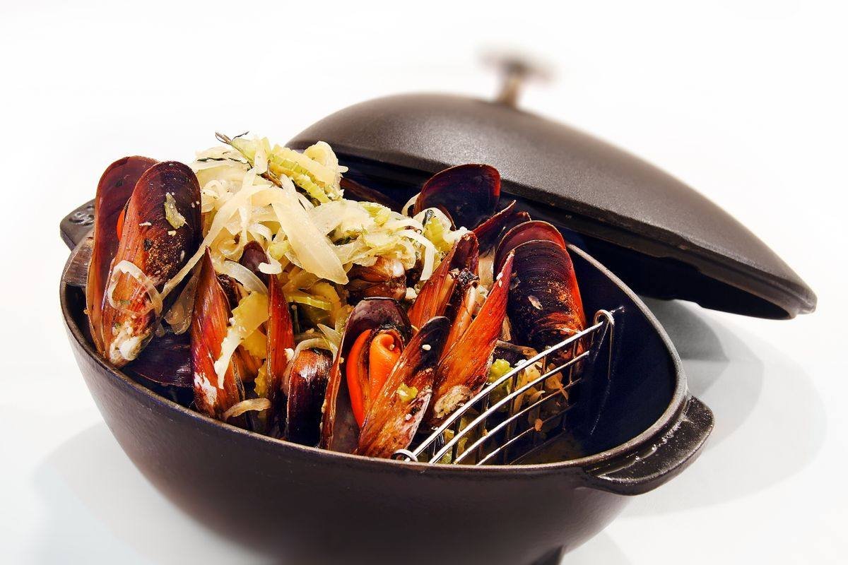 A cast iron pot of steamed mussels with leeks