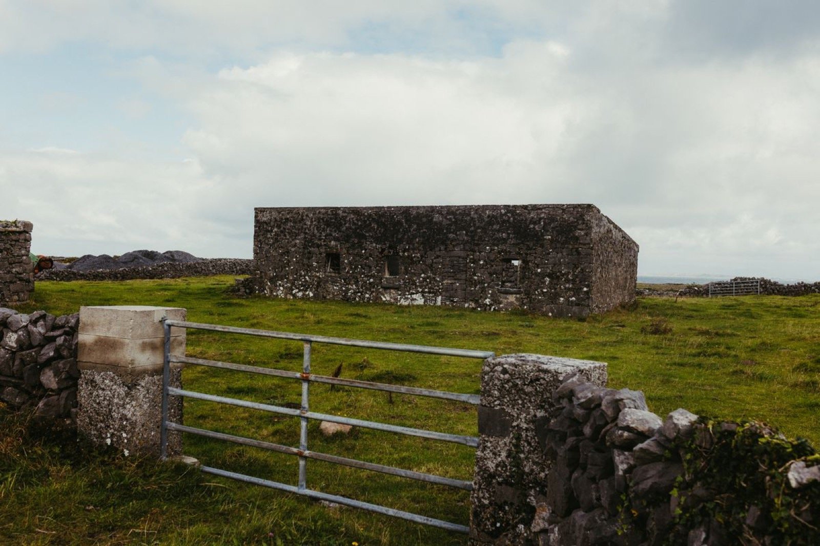 An old stone ruin behind dry-stone walls on an empty green field