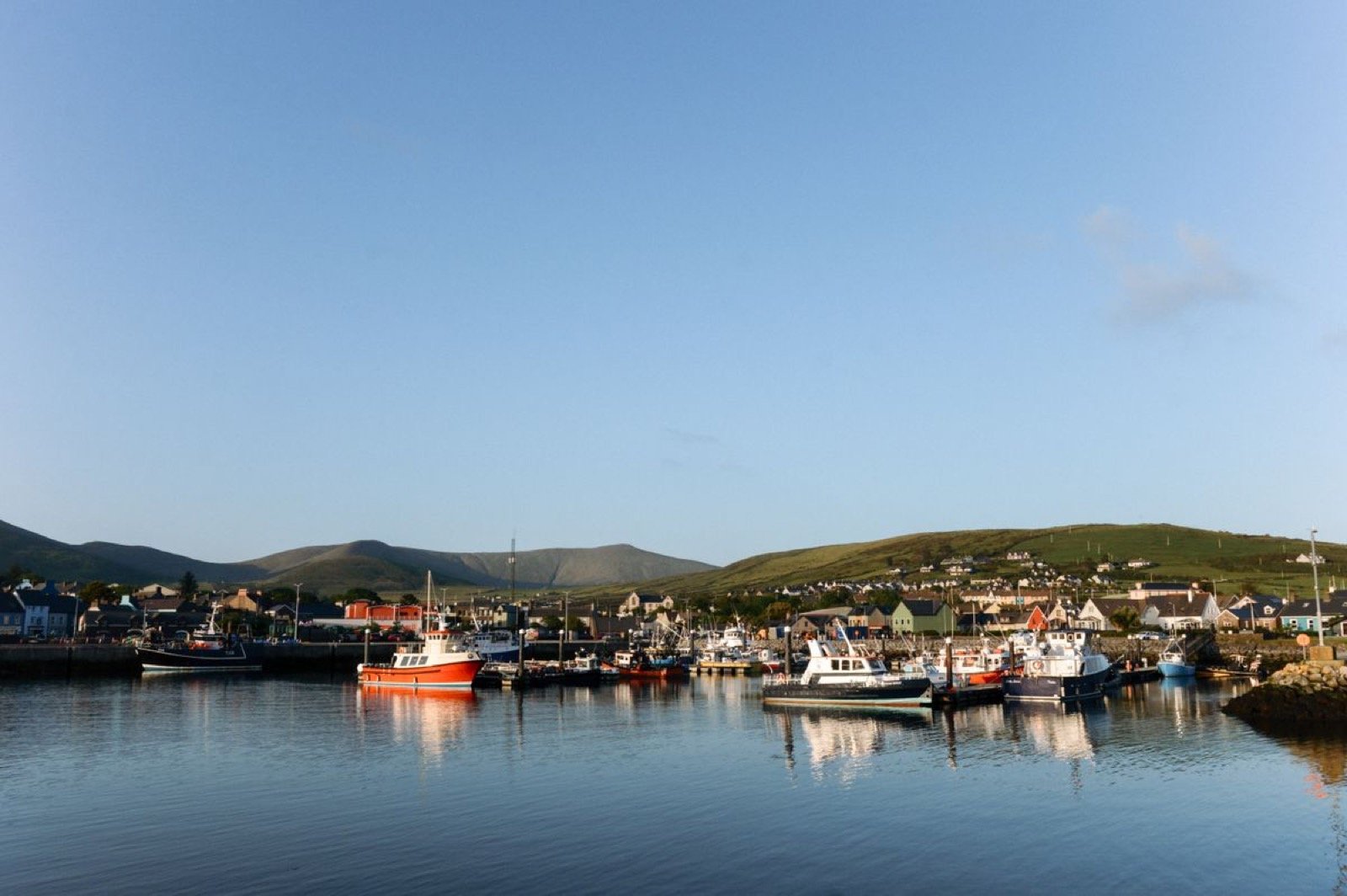 Fishing boats moored in an Irish harbour in golden light with the village behind