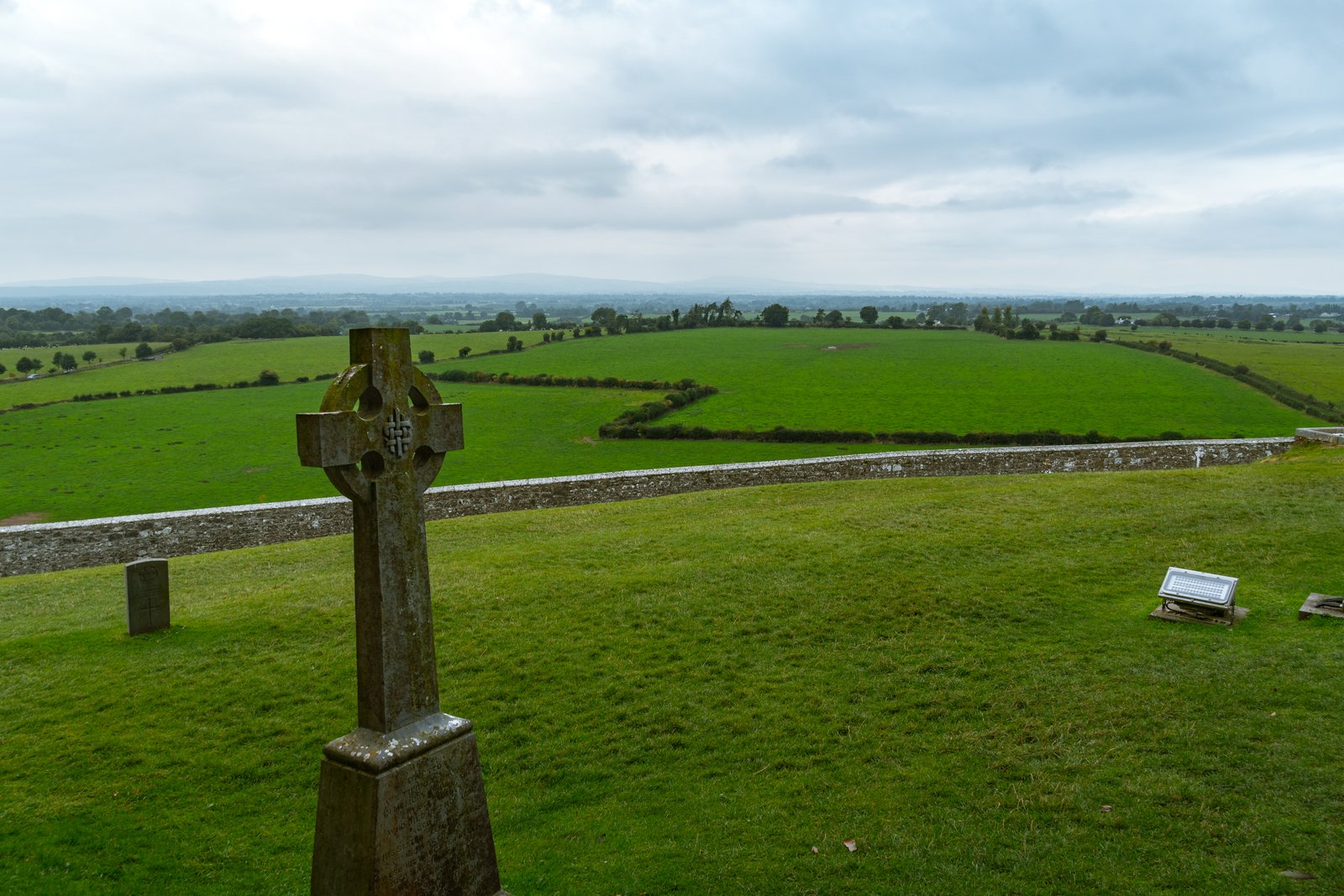 A high cross at the Rock of Cashel with the Tipperary plain behind it